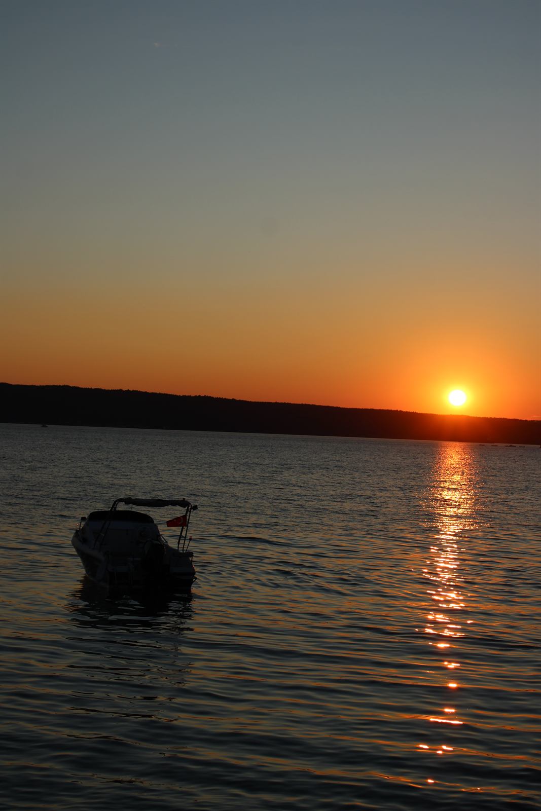 Orange sunlight reflected on the sea beside a boat silhouette at sunset